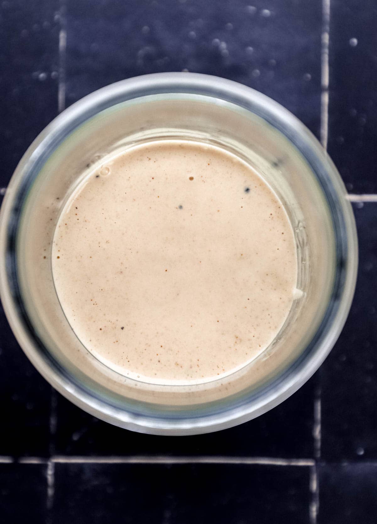 Overhead view of jar with sauce in it on black tile surface. 