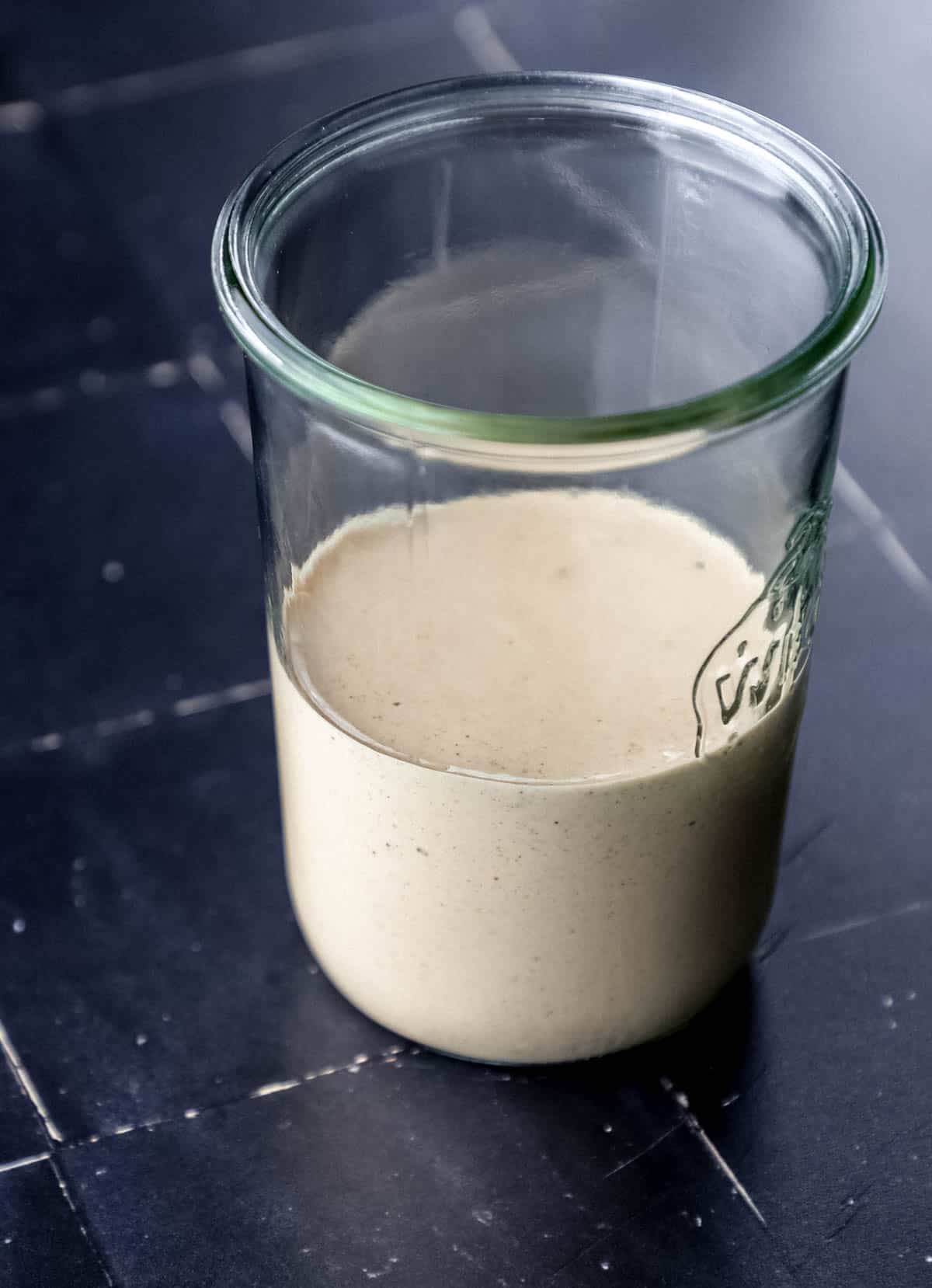 Close up side view of yum yum sauce in jar on black tile surface. 