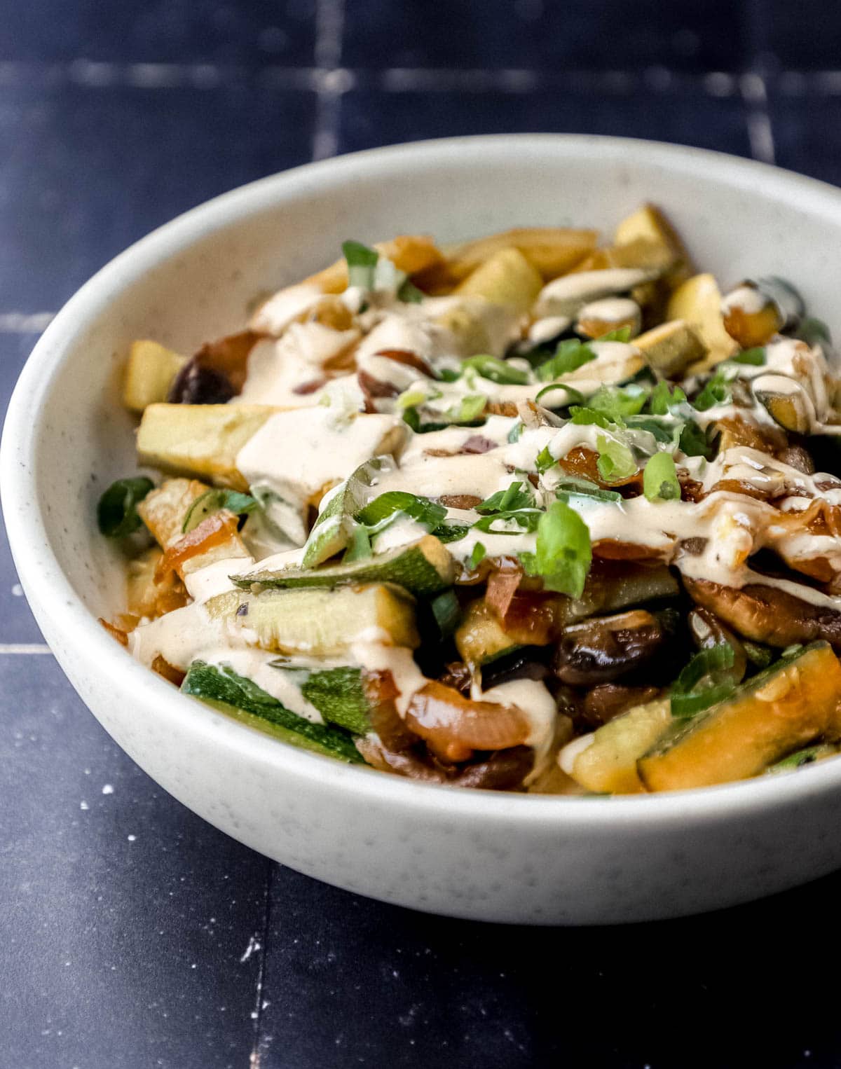 Close up side view of bowl of vegetables topped with sauce on black tile surface. 