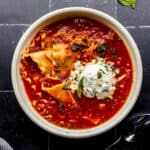 Overhead view of bowl of soup topped with ricotta mixture on black tile surface.