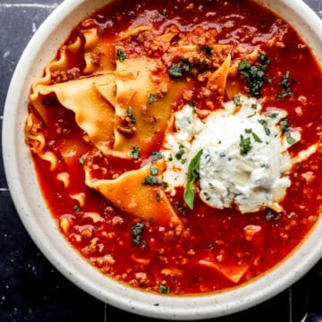 Overhead view of white bowl of lasagna soup on black tile surface.