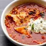 Close up side view of soup in a white bowl topped with ricotta cheese mixture.