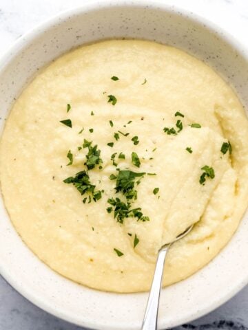 Overhead view of southern cheese grits recipe in a white bowl with spoon topped with fresh chopped parsley.