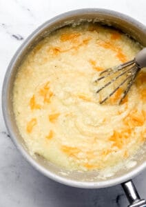 Overhead view of shredded cheese added to grits in saucepan.