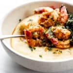 Close up side view of shrimp and grits in white bowl with spoon in it.