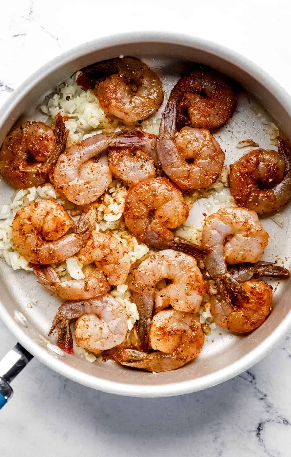 Large raw shrimp added to large skillet with onion, garlic, and olive oil. 