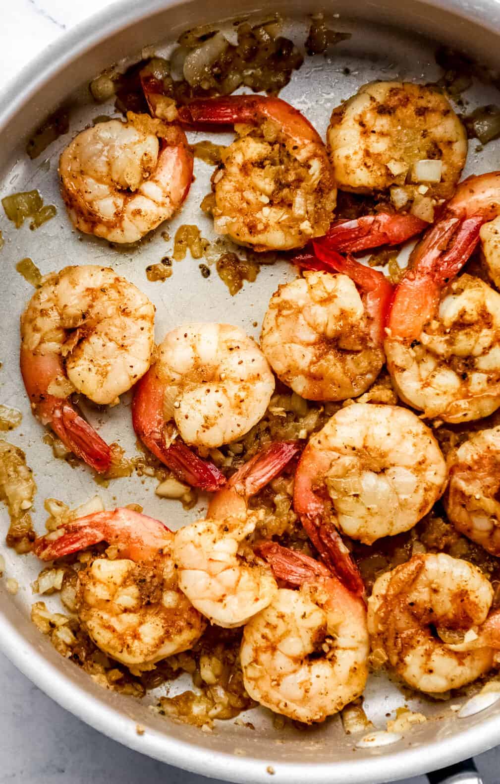 Cooked shrimp in large skillet with sauteed onion and garlic. 