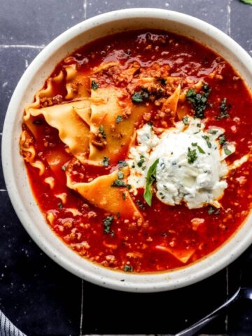Overhead view of white bowl of lasagna soup on black tile surface.