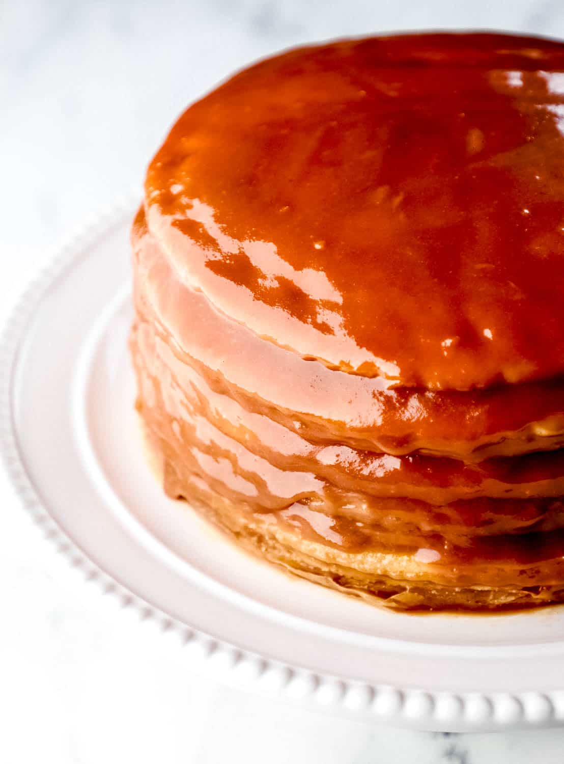 Close up side view of whole cake topped with chocolate icing on white cake plate. 