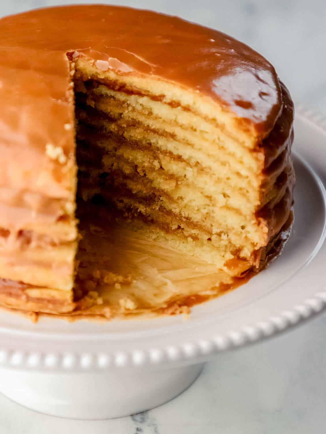 Close up side view of whole cake with slice taken out of it on white bake plate. 