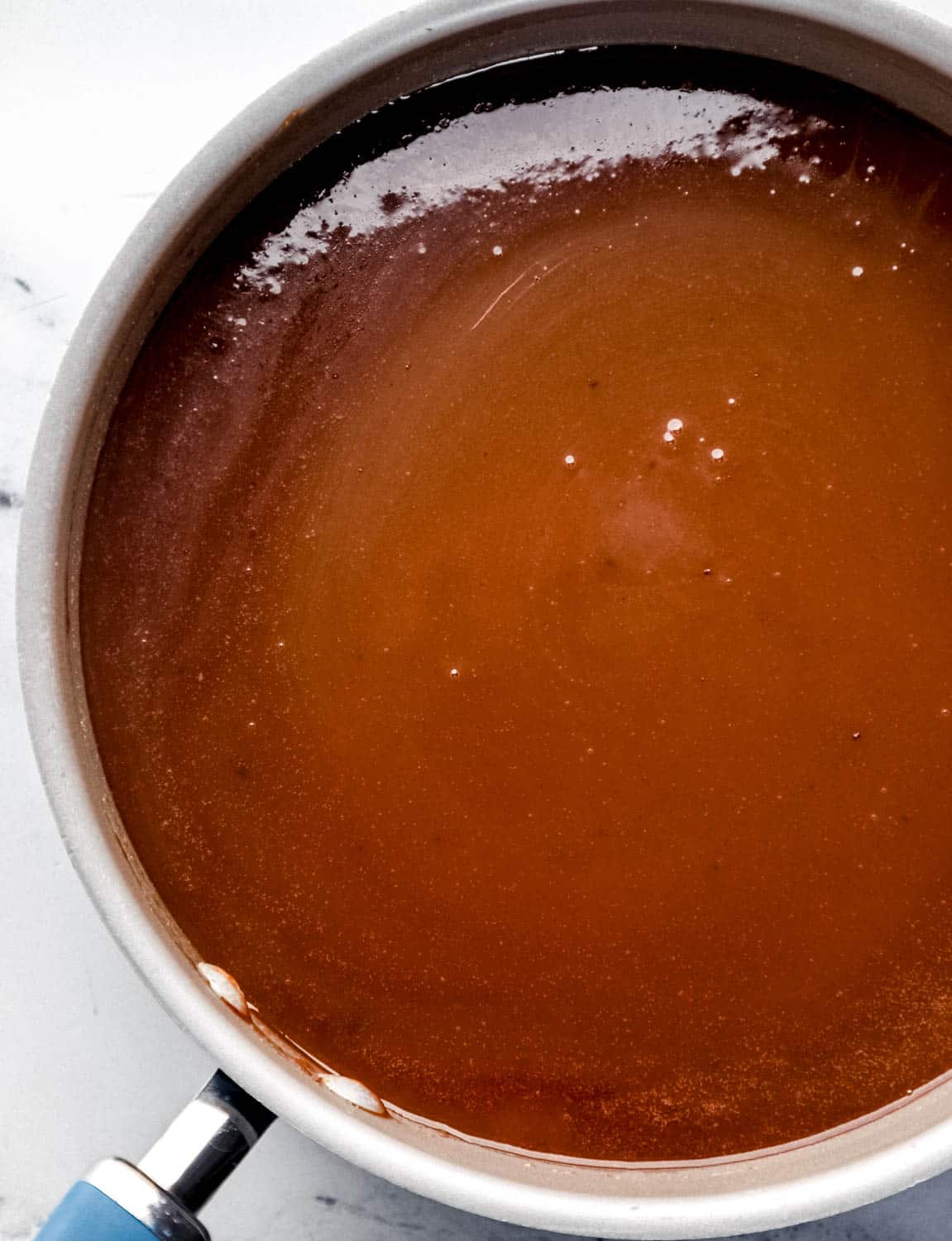 Overhead view of ingredients to make chocolate icing combined in large skillet. 