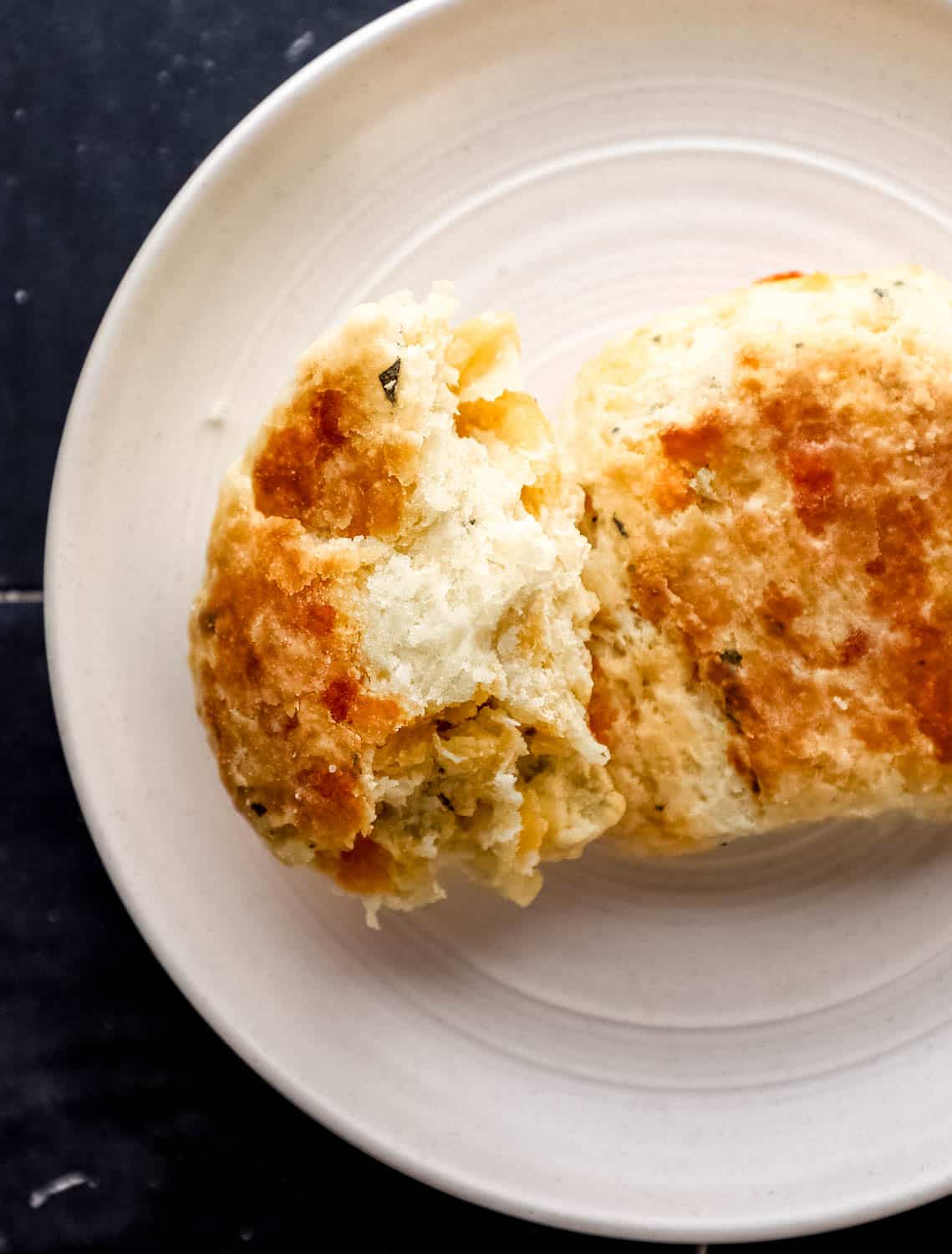 Close up view of two biscuits on white plate with one cut in half. 