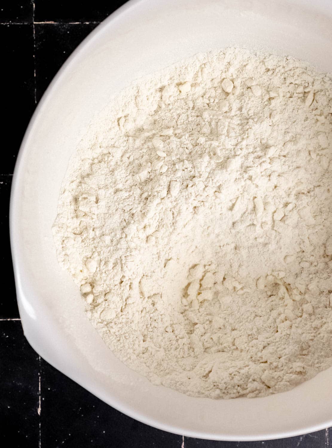 Overhead view of large white mixing bowl with dry ingredients and butter combined in it. 