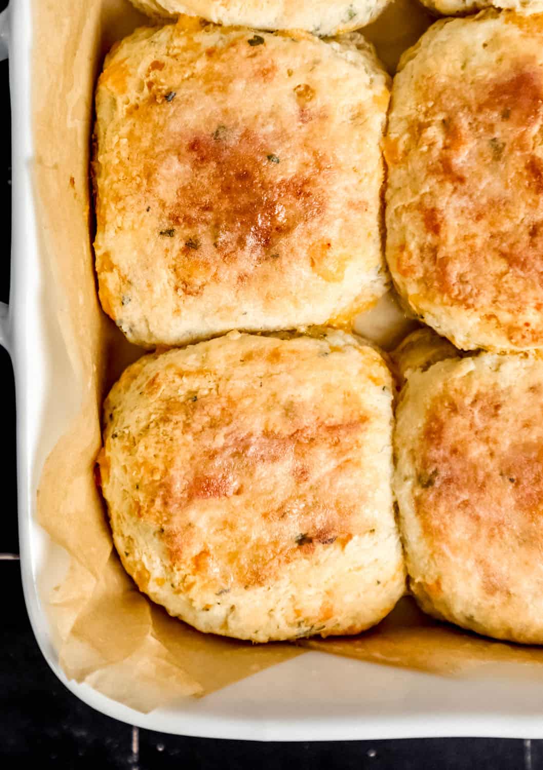 Close up view of baked biscuits in white parchment lined baking dish on black tile surface. 