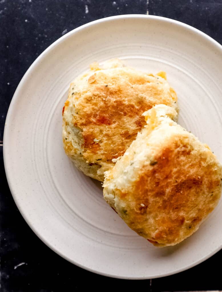 Two cheddar biscuits on a white plate on black tile surface.