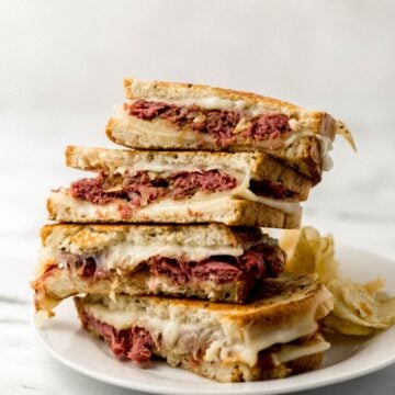 Close up side view of two grilled cheese sandwiches stacked on top of each other on white plate with chips on it.