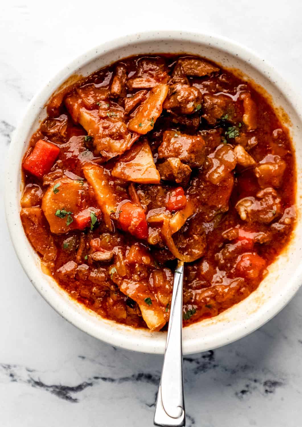 Bowl of stew with spoon in it on marble surface. 