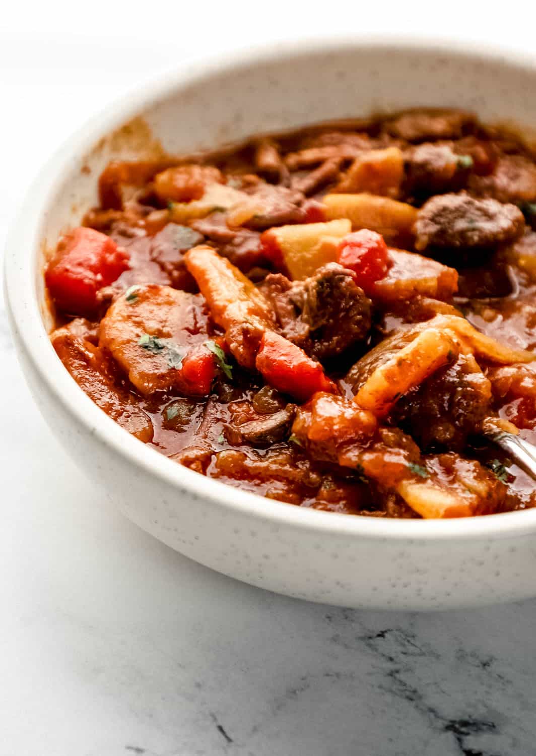 Close up side view of bowl of stew on marble surface. 