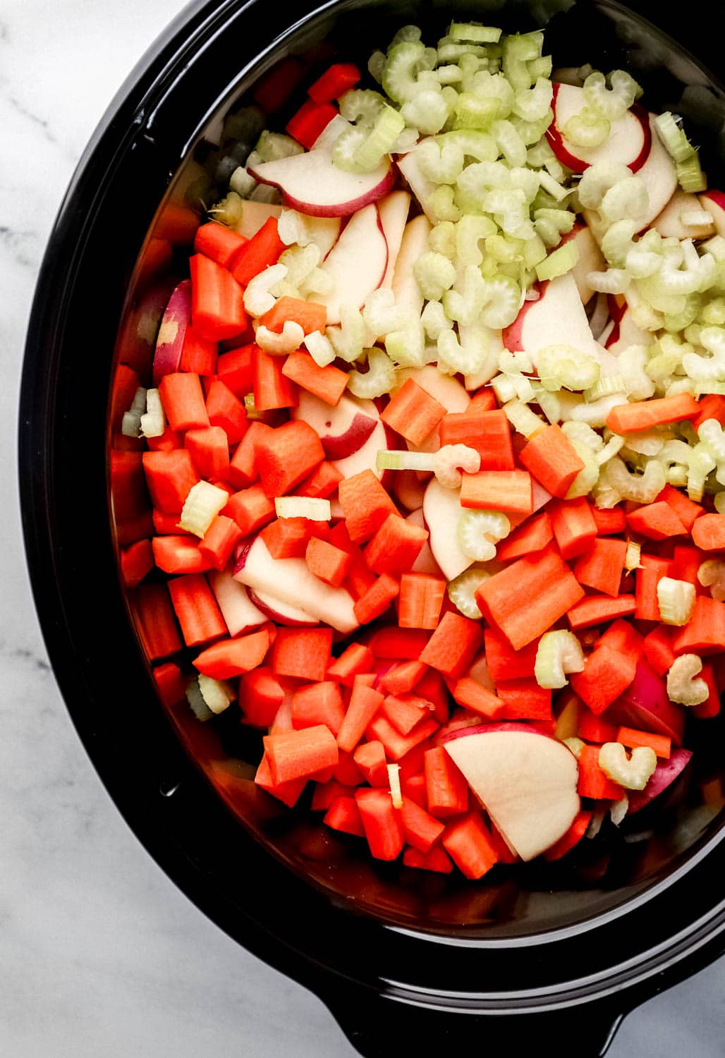 Potatoes, celery, and carrots added to crock pot with onion and beef. 