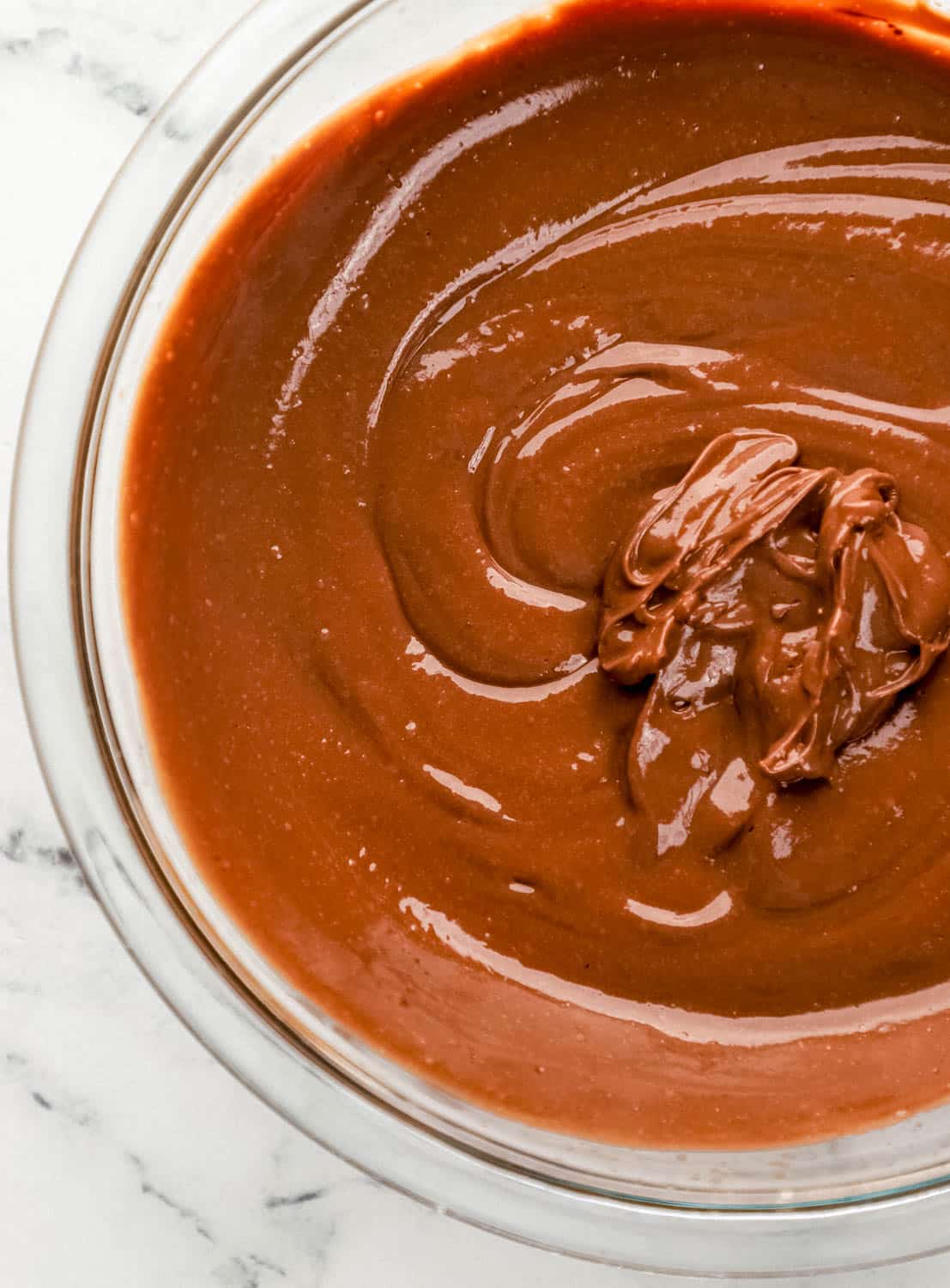 Chocolate pudding in large glass mixing bowl on marble surface. 