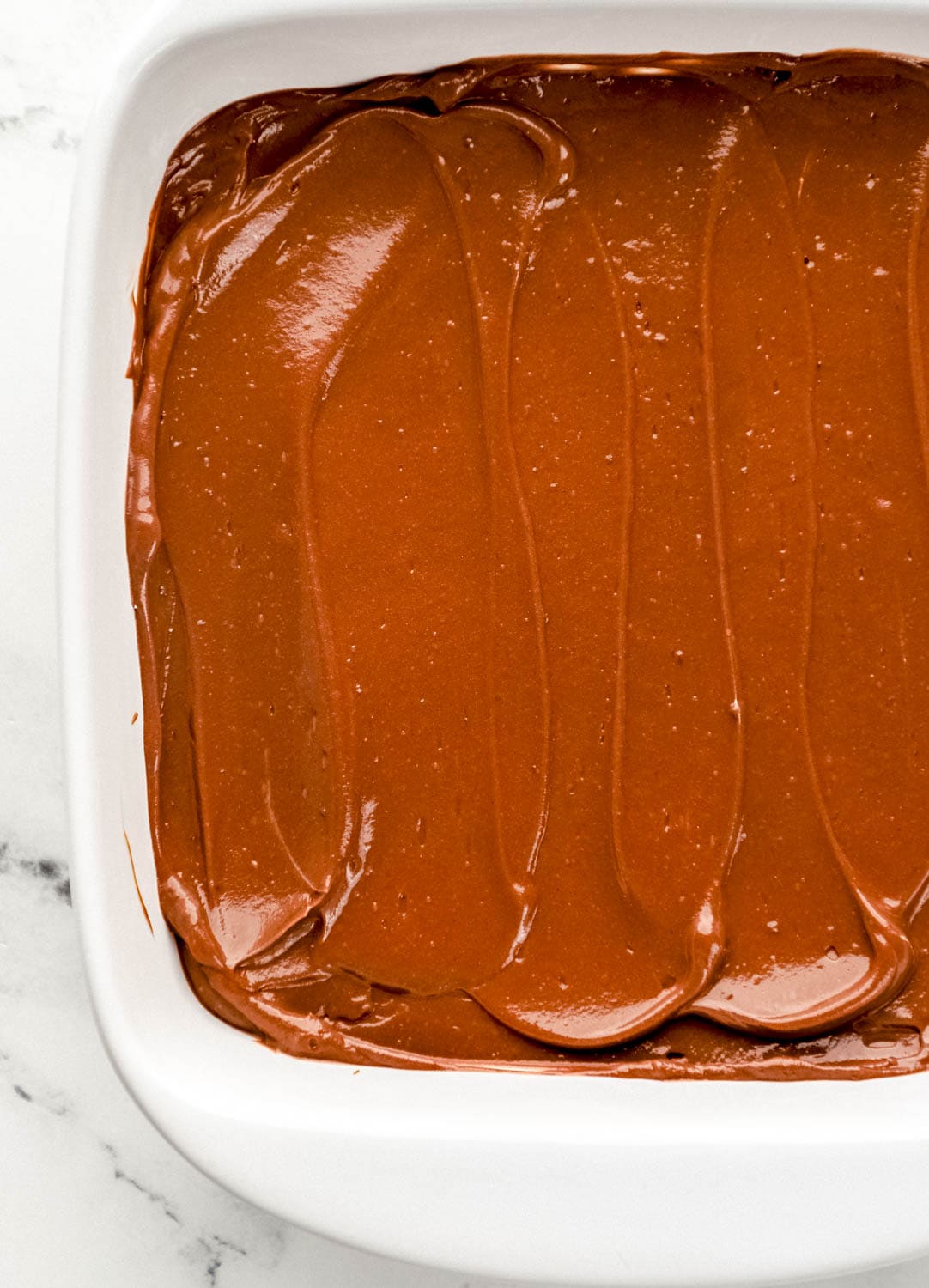 Chocolate pudding spread into the bottom of a square white baking dish. 