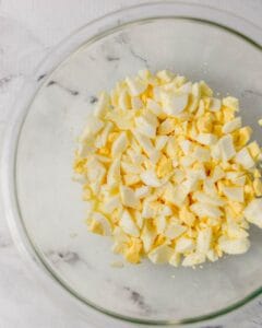Chopped eggs in a large glass mixing bowl.