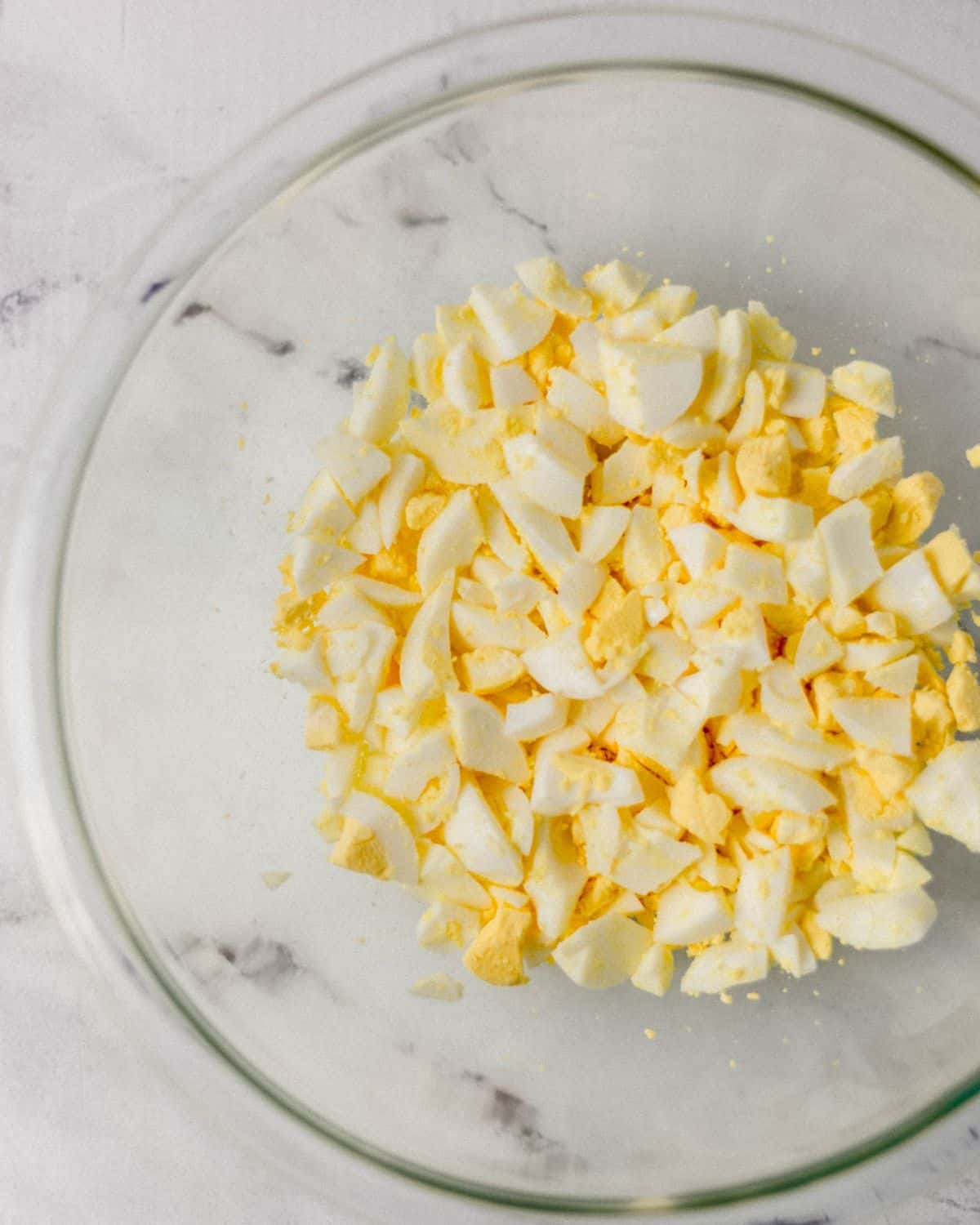 Overhead view of chopped up hard boiled eggs in large glass mixing bowl. 