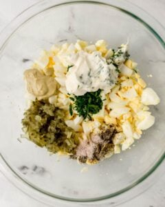 Egg salad ingredients added to large glass mixing bowl.