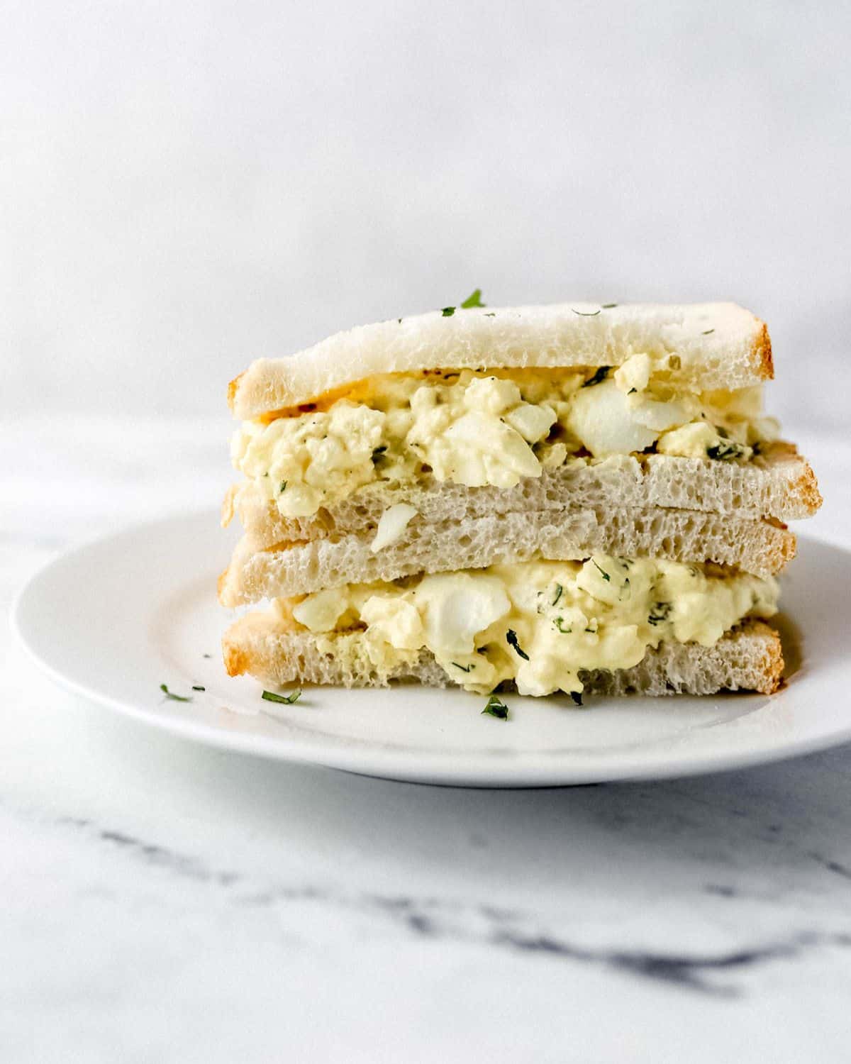 Close up side view of egg salad sandwich on white plate. 