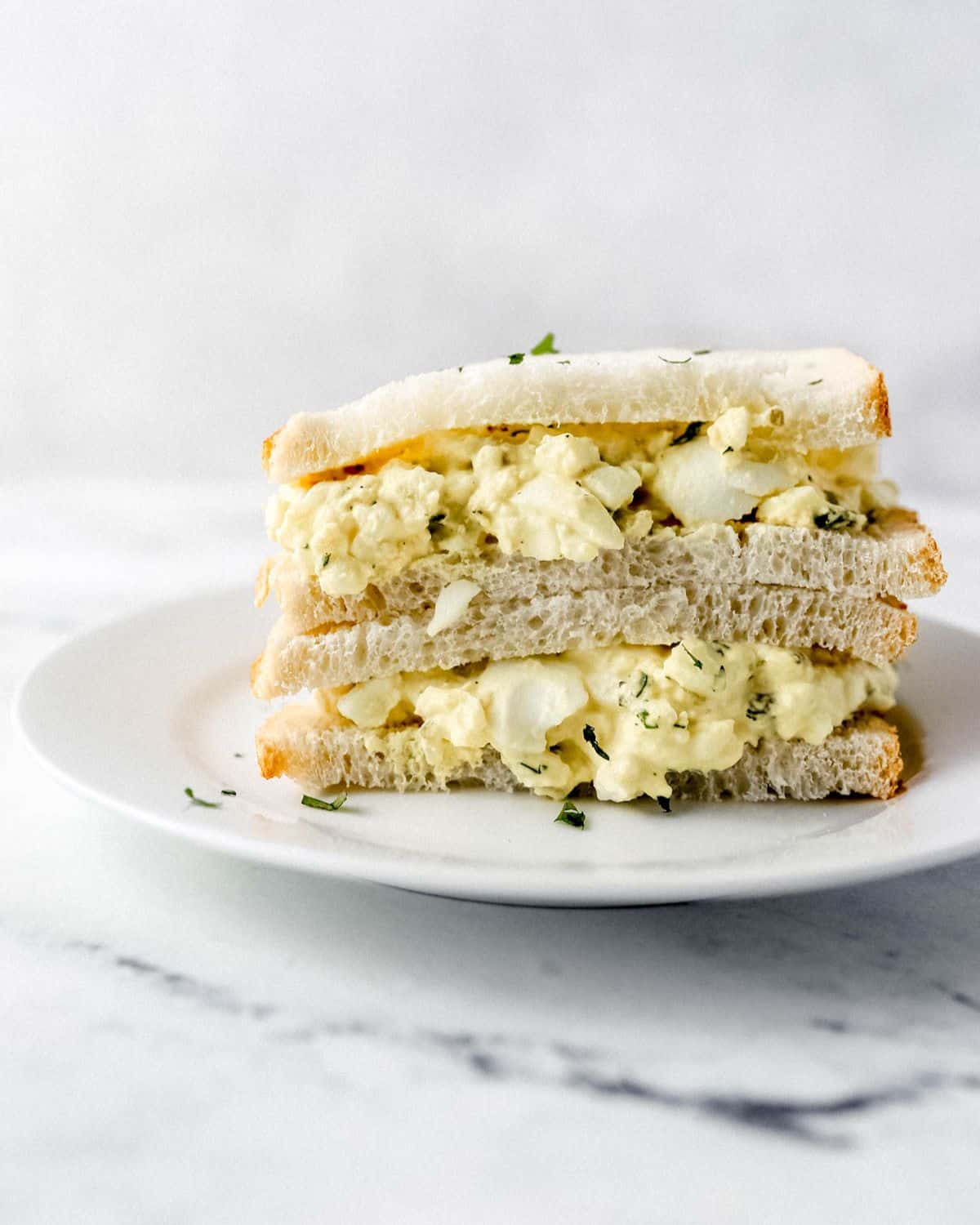 Close up side view of egg salad sandwich on white plate.
