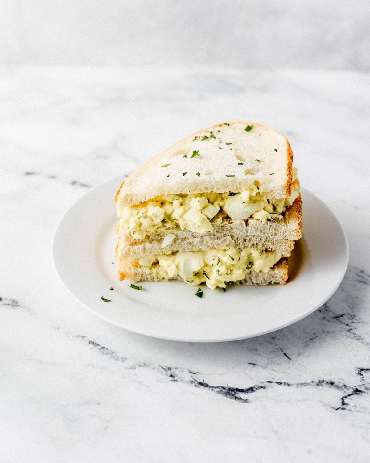 Egg salad sandwich cut in half and stack on white plate. 
