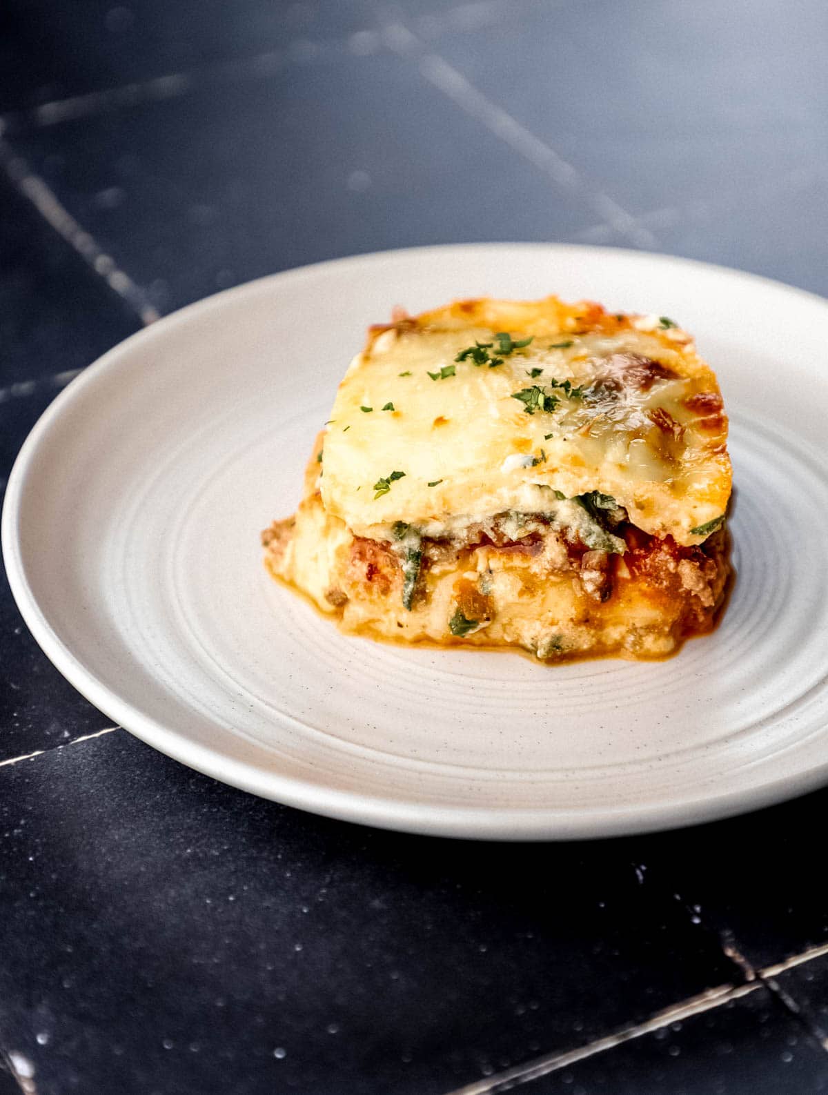 Close up side view of single serving of lasagna on white plate. 