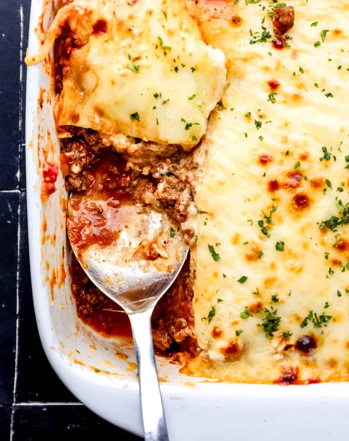 Overhead view of lasagna in baking dish with a piece out of it with serving spoon in it. 