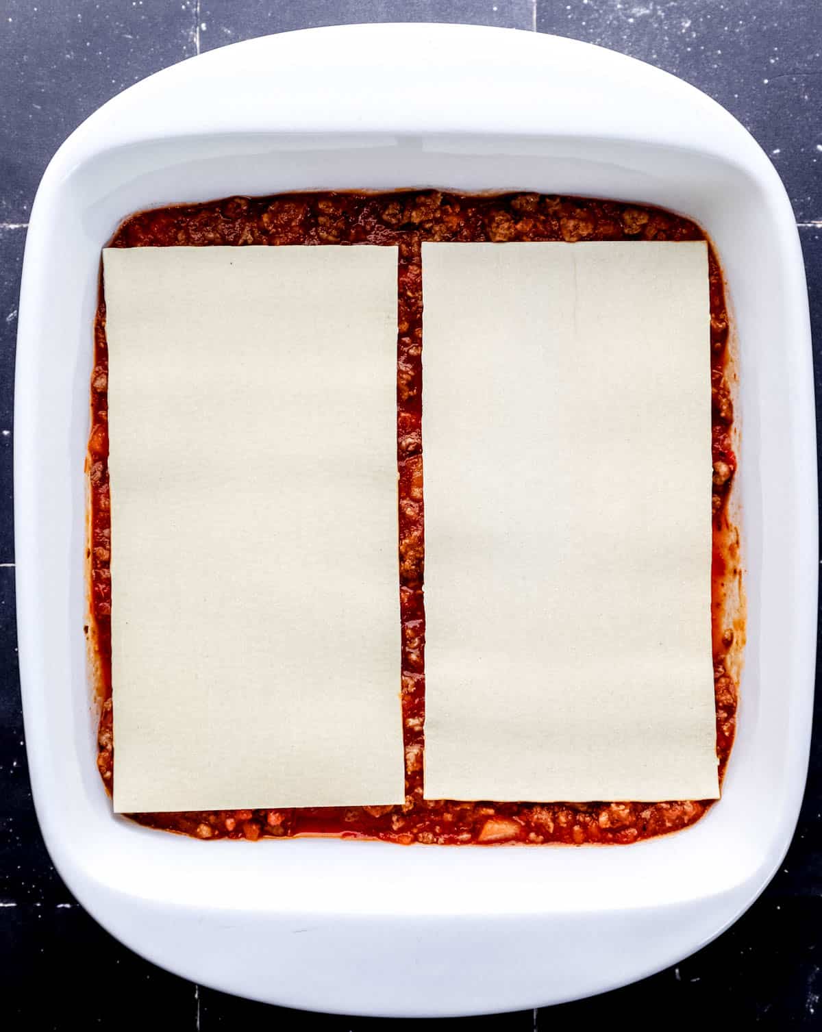 Overhead view of square white baking dish with meat sauce and lasagna noodles in it. 