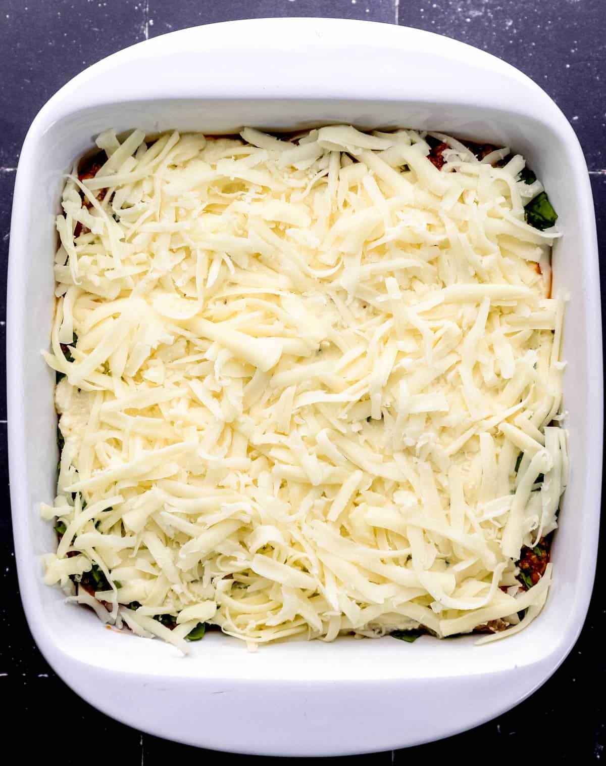 Overhead view of white baking dish with first full layers of lasagna in it. 