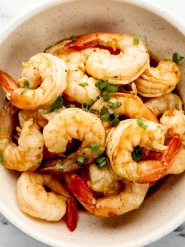 Overhead view of bowl of hibachi shrimp in white bowl topped with sliced green onion on marble surface.