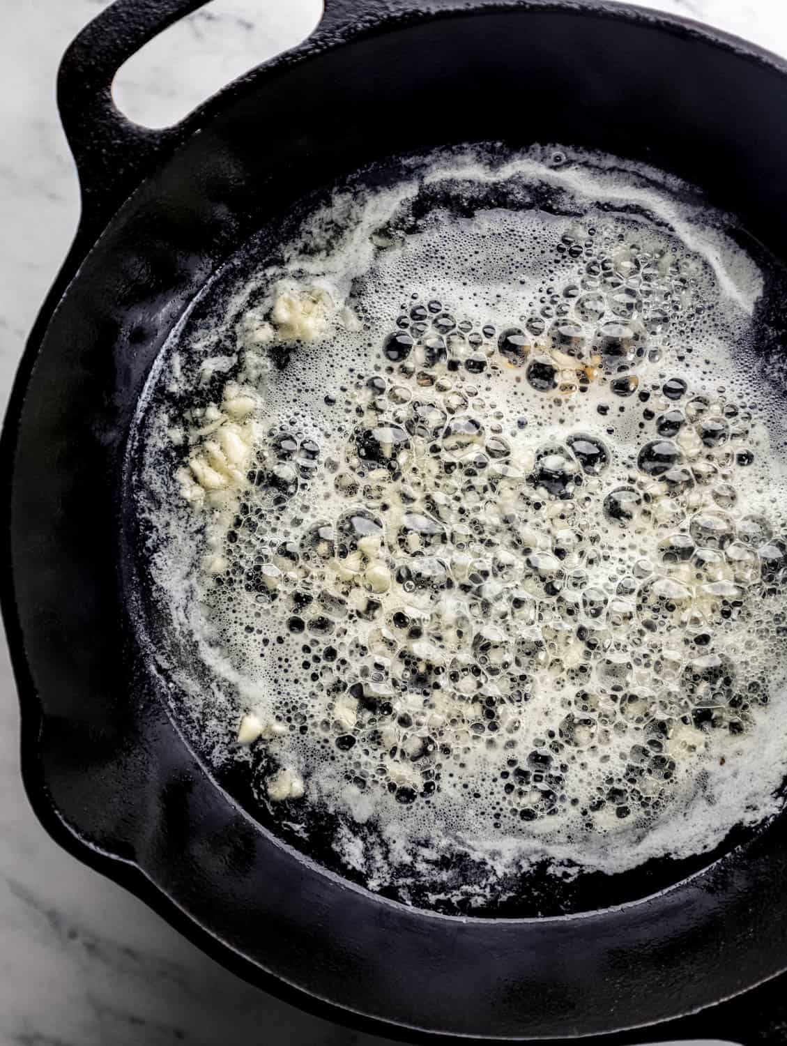 Overhead view of cast iron skillet with oil, butter, and garlic in it. 