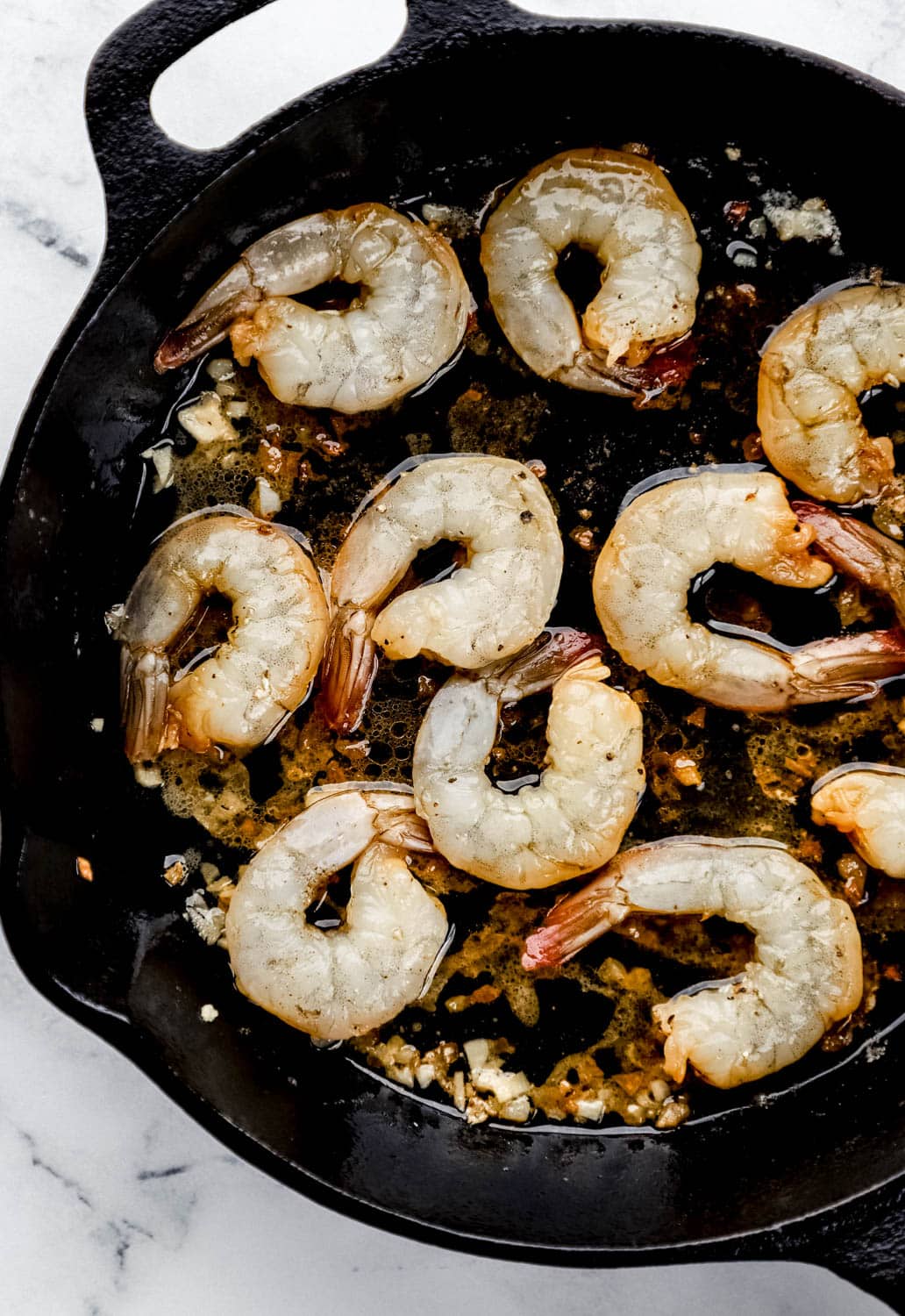 Shrimp added to cast iron skillet with butter, oil, and garlic in it. 