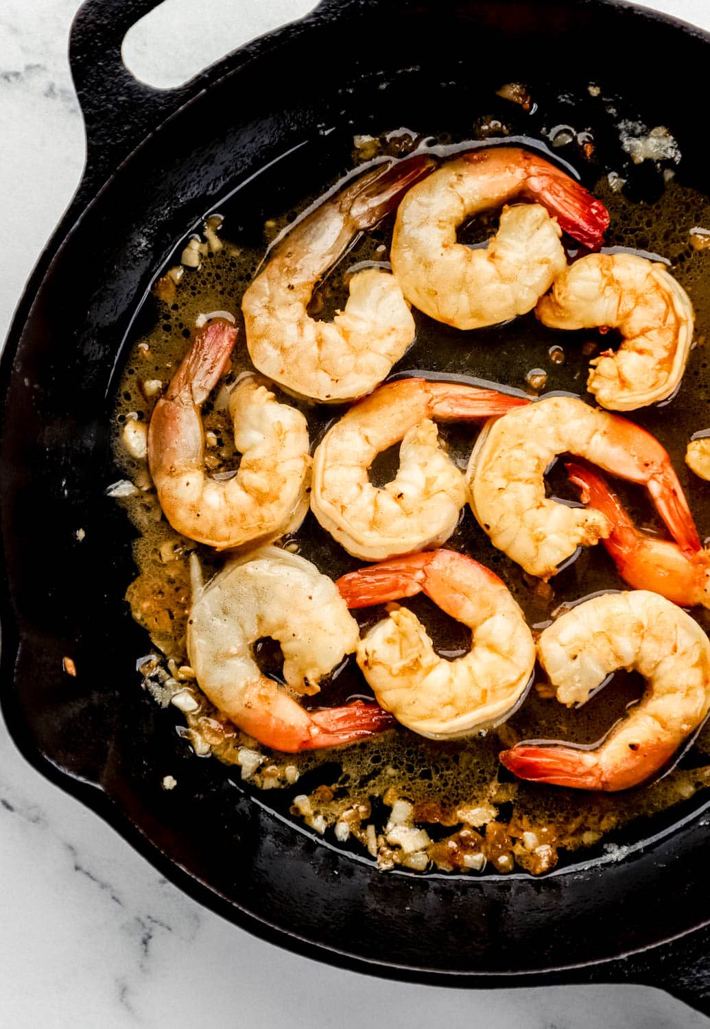 Overhead view of cooked shrimp in cast iron skillet with other ingredients. 