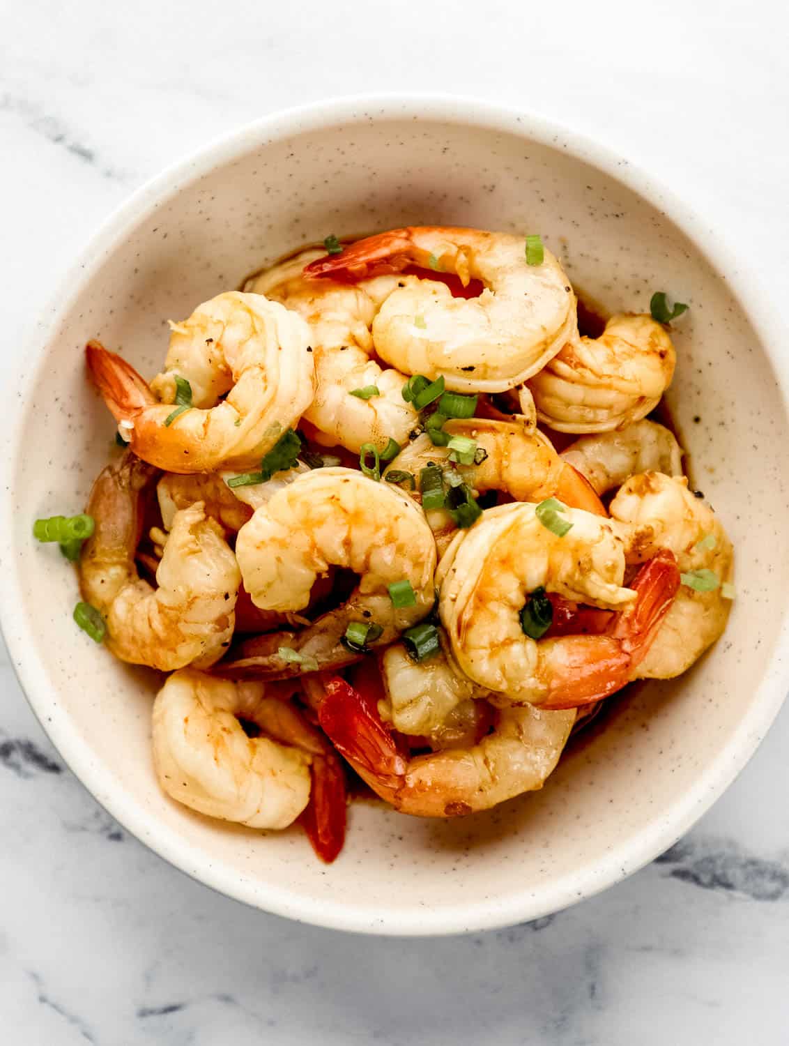 Overhead view of hibachi shrimp in white bowl topped with sliced green onion. 