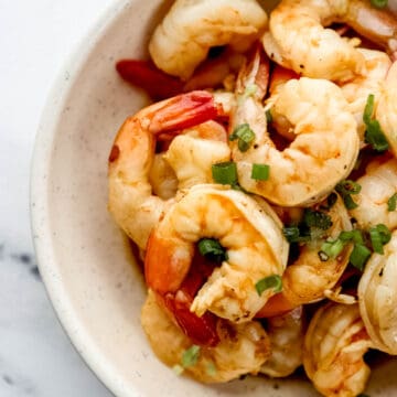 Close up view of hibachi shrimp topped with green onion in white bowl.