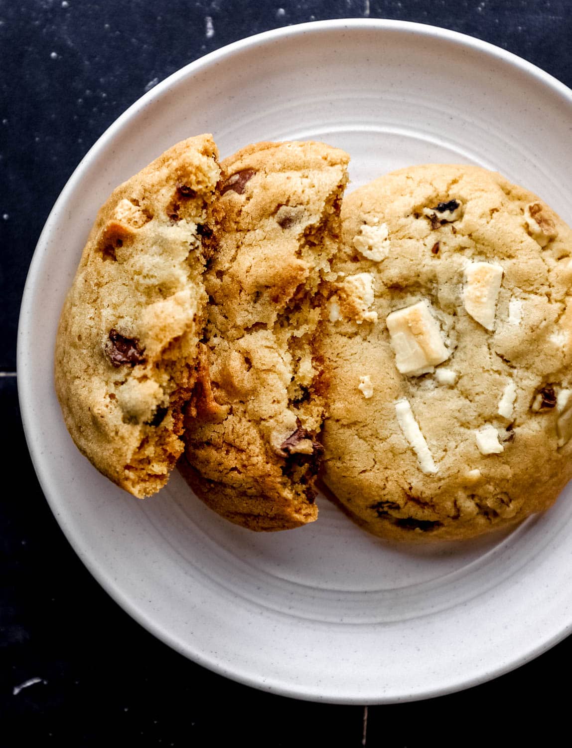 Overhead view of two baked cookies on white plate with one broke in half. 