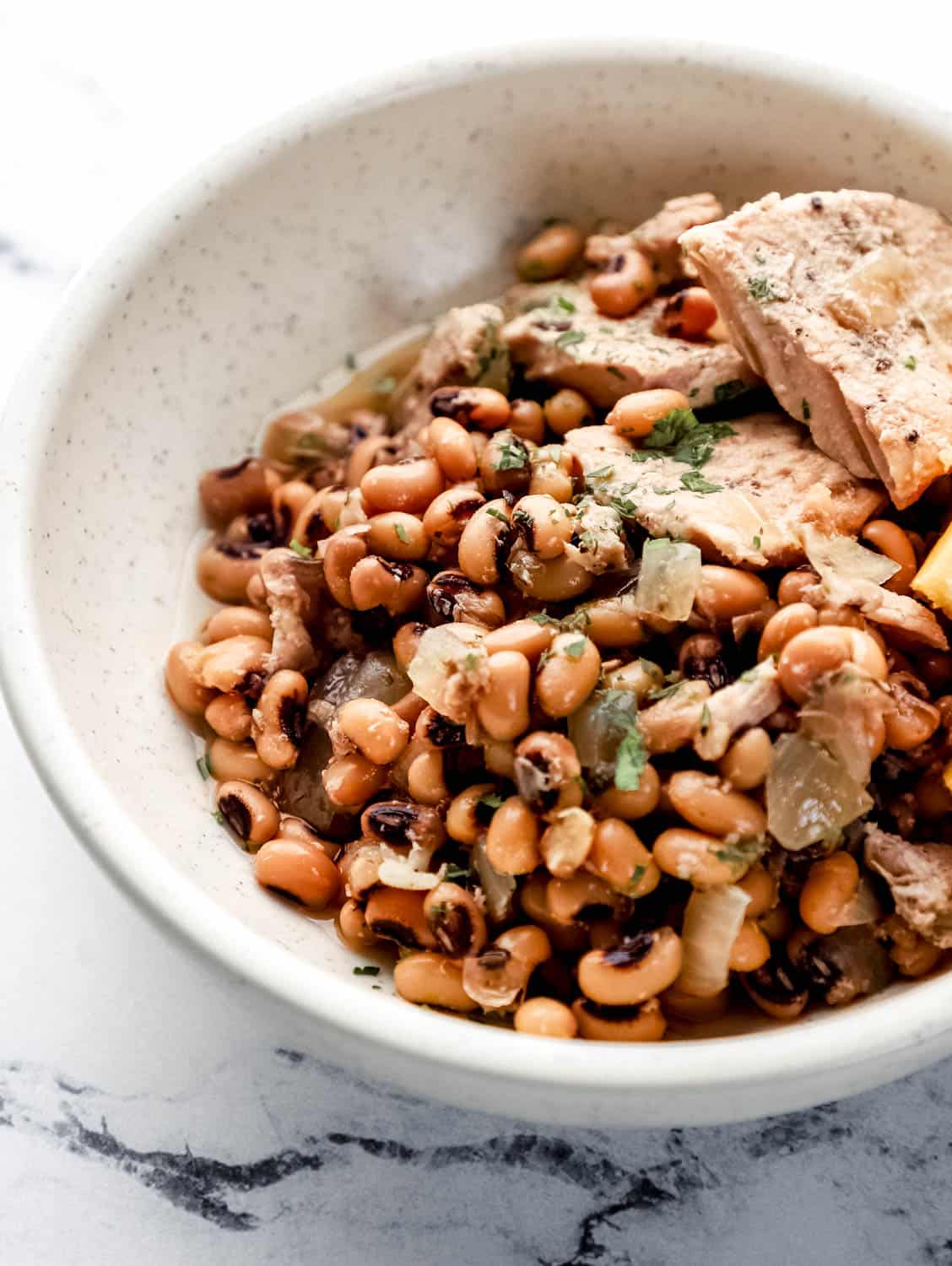 Close up side view of bowl with beans and meat in it on marble surface. 