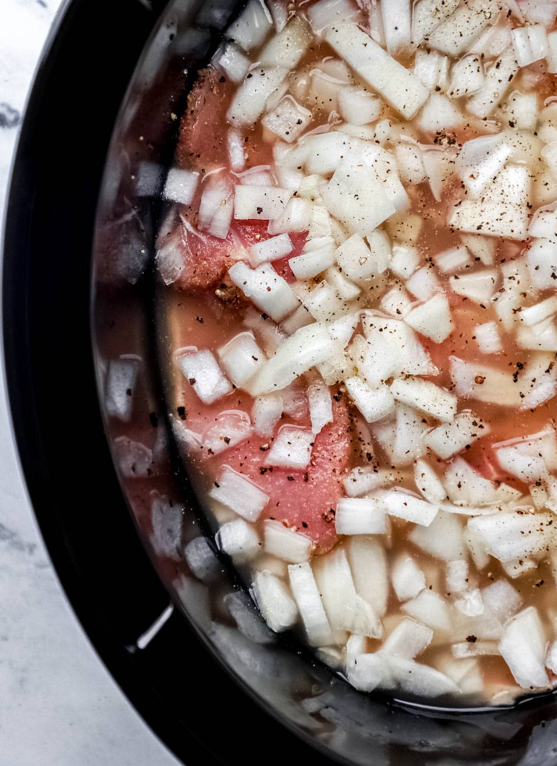 Beans, pork chops, and chopped onion in black slow cooker. 