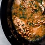 Black slow cooker with finished black eyed peas and pork chops topped with fresh chopped parsley.