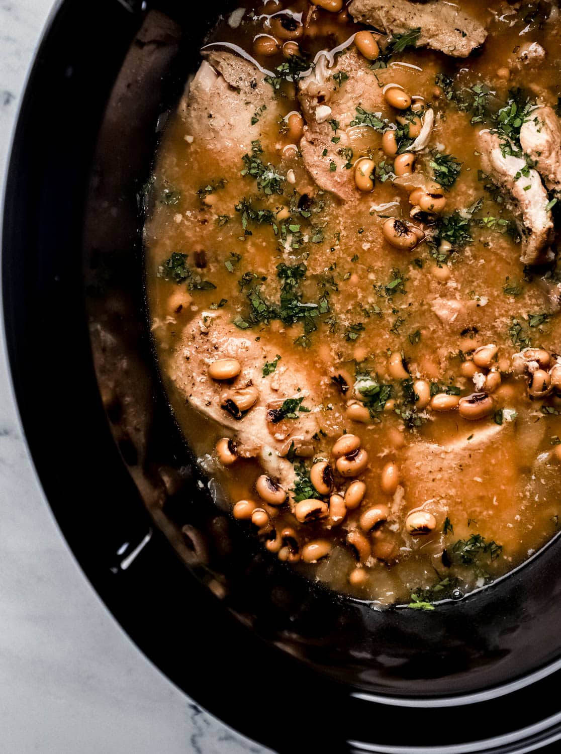 Close up overhead view of finished beans and pork chops in slow cooker topped with freshly chopped parsley. 