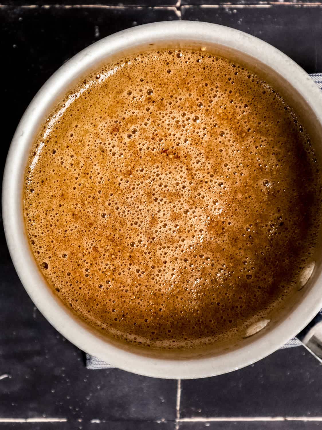 Glaze ingredients combined in saucepan on black tile surface. 