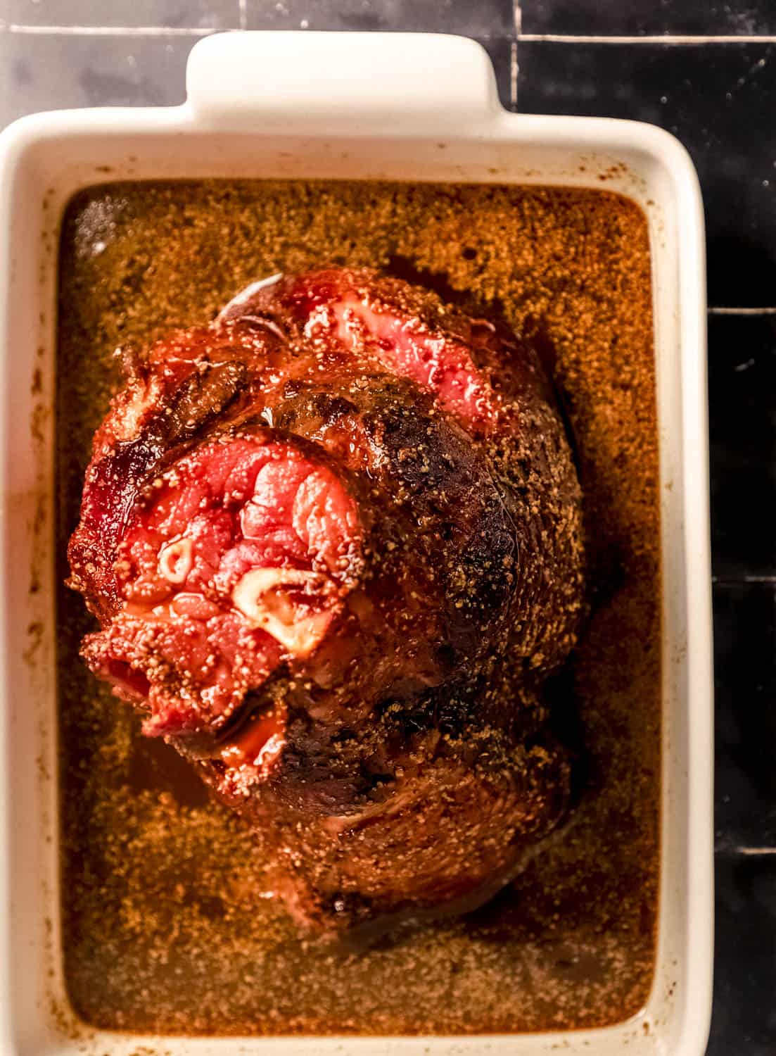 Overhead view of ham covered in glaze in roasting pan. 