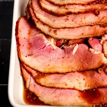 Close up front view of sliced ham in white baking dish.