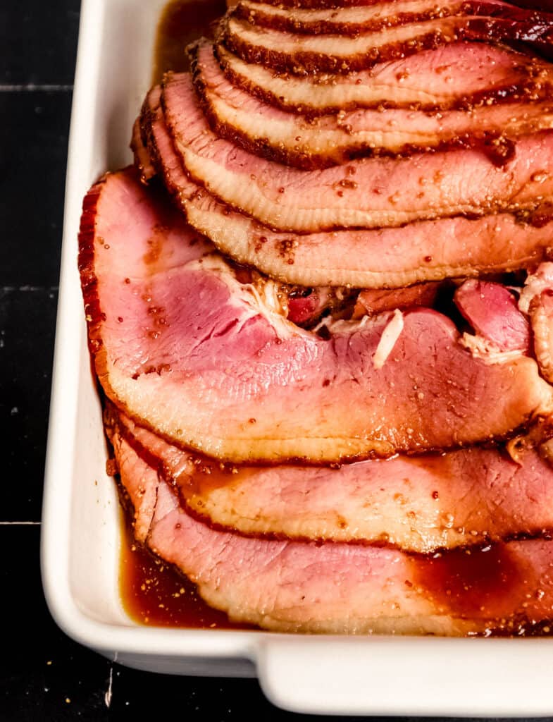 Close up front view of sliced ham in white baking dish.